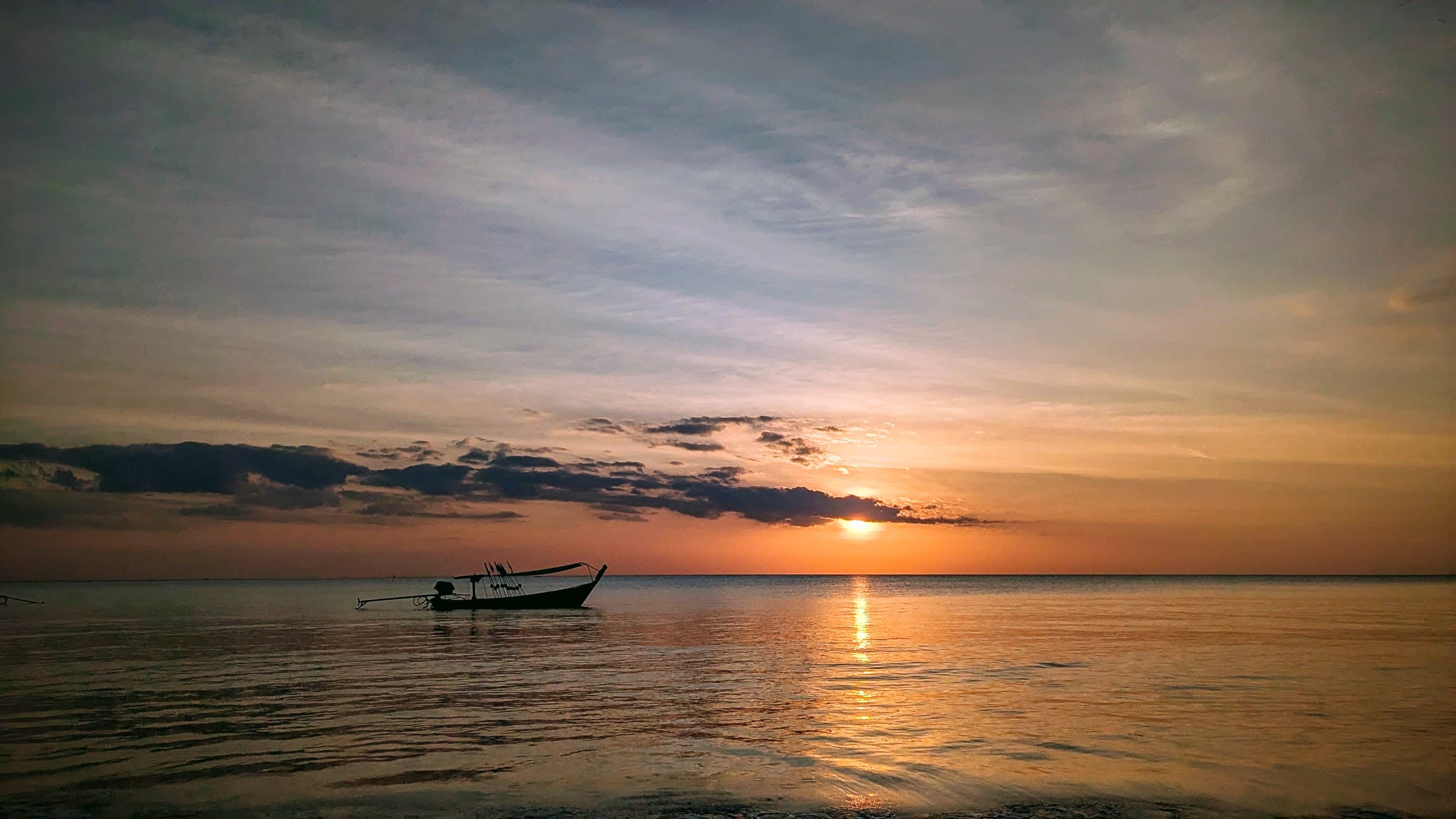 A lone boat silhouetted against a golden sunset over calm waters